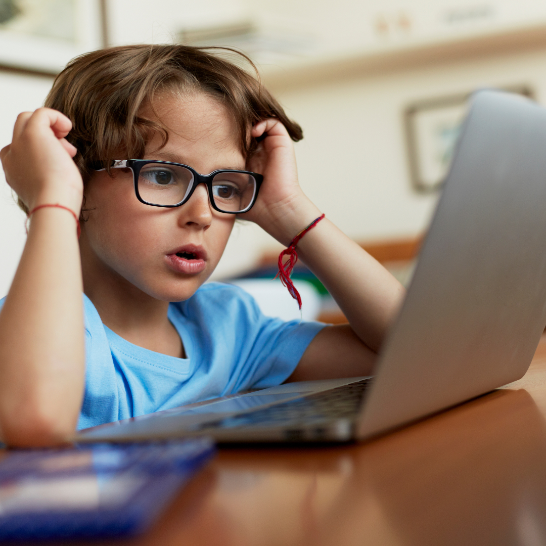 A young boy with thick glasses sits at a laptop