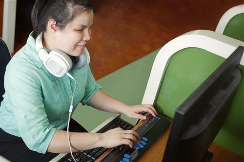 Asian young blind woman with headphone using computer with refreshable braille display or braille terminal a device