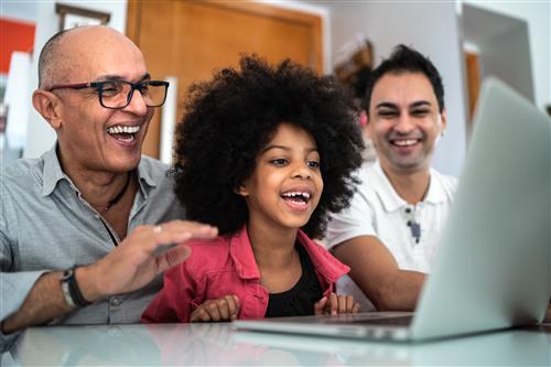two fathers look over their daughter's shoulder as she smiles at a laptop