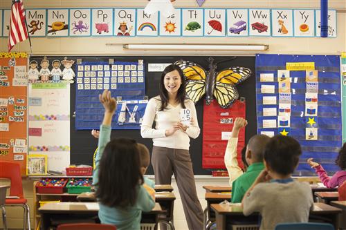 teacher standing in front of the classroom with students raising their hands