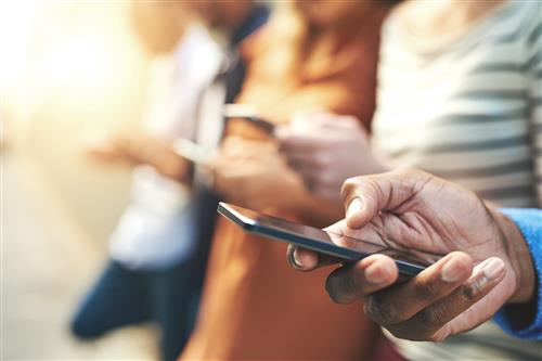 a man's hands hold a phone. In the background more people are holding their phones